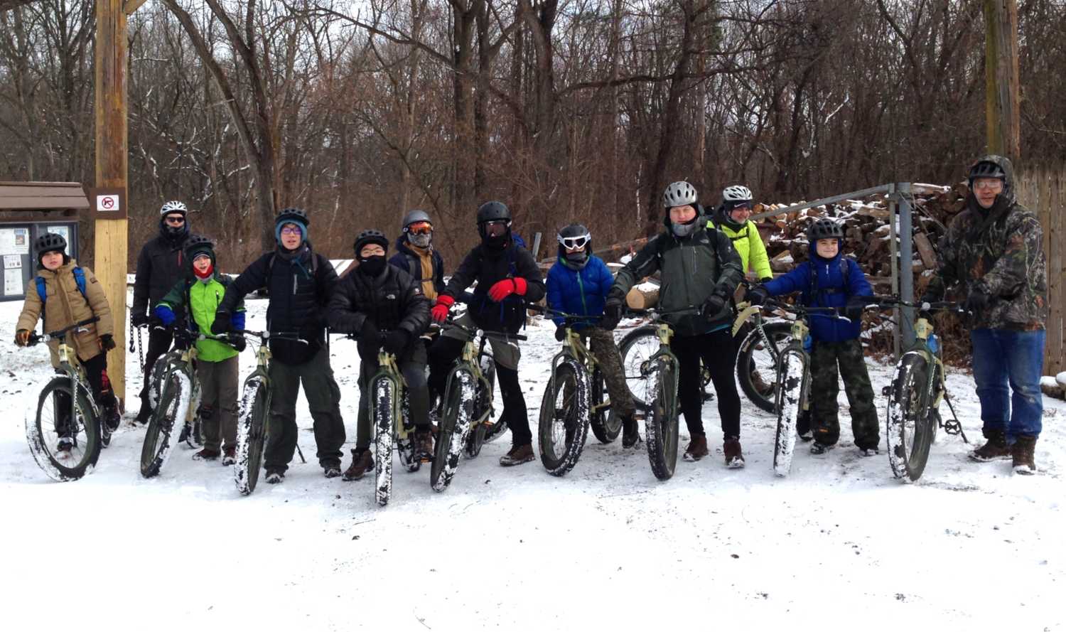 A group of scouts on bikes line up for a camera shot in the snow.